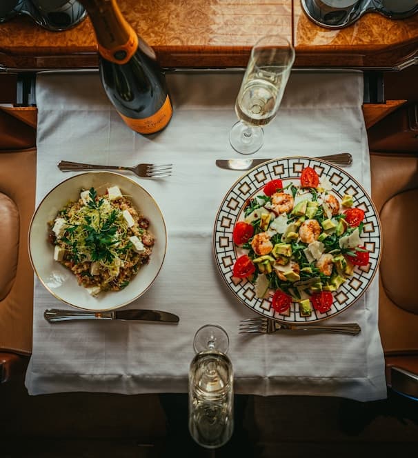 Overhead view of plated dishes and champagne on a private-jet dining table